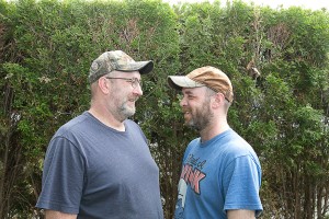Wesley and Thomas were married May 11, 2015, Billerica, MA. Here, they are facing each other in front of shrubs.